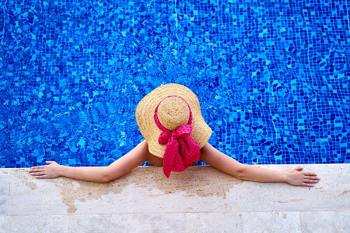 Lady wearing sun hat looking out into a calm swimming pool taken from above