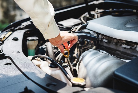 A car engine with an arm reaching for the oil dipstick on a sunny day