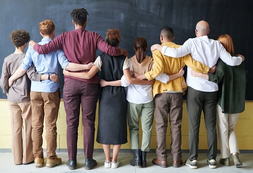 Rear view of line up of people with arms over each others shoulders facing a blackboard