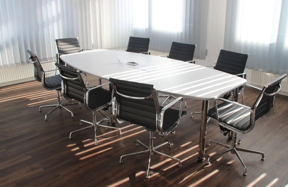 Empty conference room with white table, black chairs and sunlight piercing closed blinds