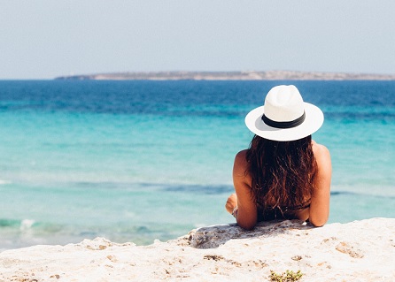 A Women with a white hat lays facing a blue ocean