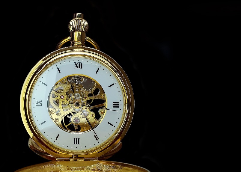 Golden pocket watch with white face and visible mechanism offset against a black background 