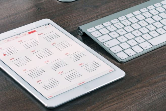 Modern Keyboard and tablet displaying a calendar placed on a dark wood desk